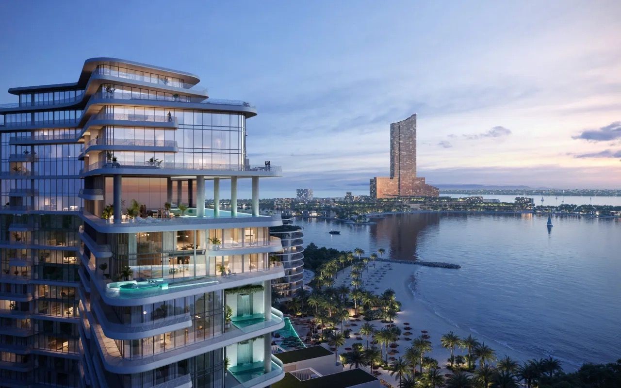 Modern glass high-rise building overlooking a tranquil waterfront, with distant city skyline and sunset sky.